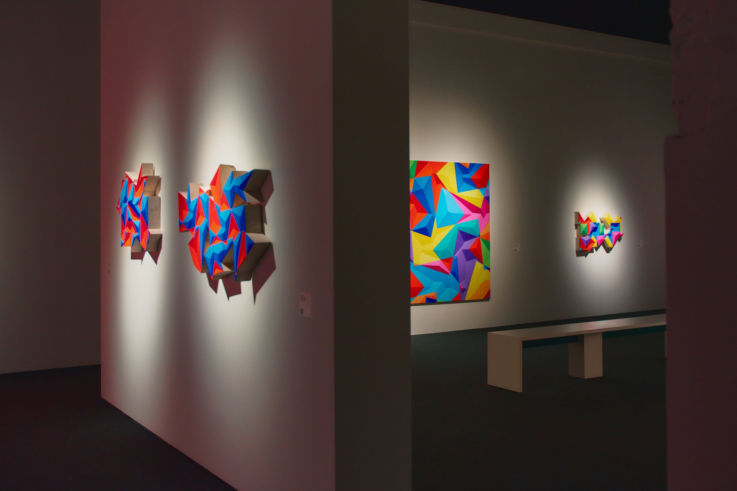 Sala de l'exposició amb relleus facetats i una tela geomètrica de colors vius de Petr Kvíčala
